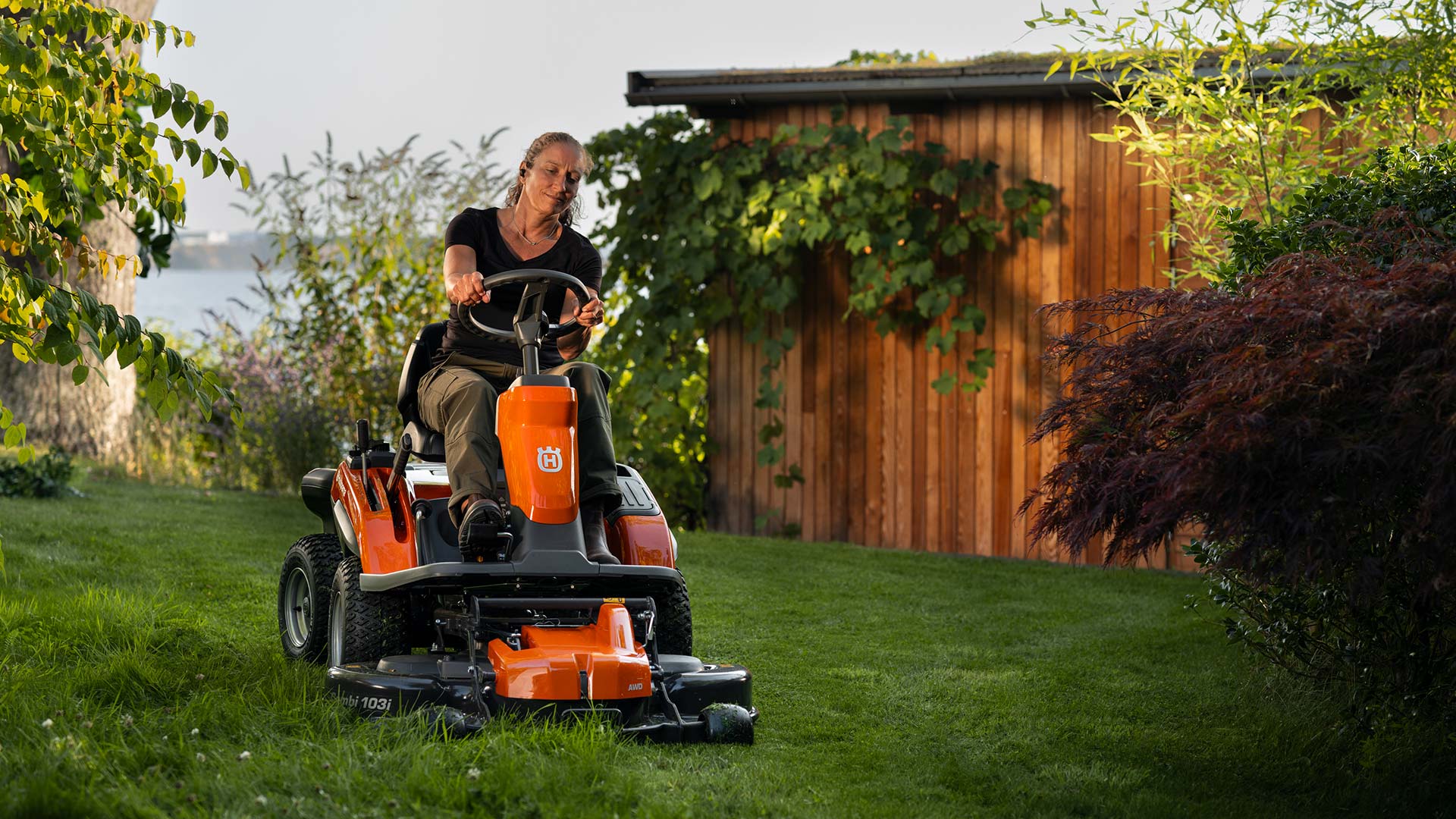 Eine Person fährt konzentriert auf einem orangefarbenen Rasenmäher im Garten.